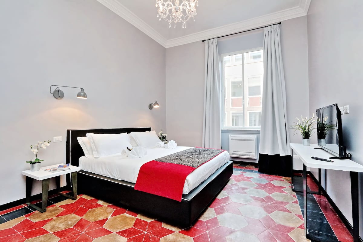 A modern hotel room with a bed, bedside table, TV, and a window with curtains.