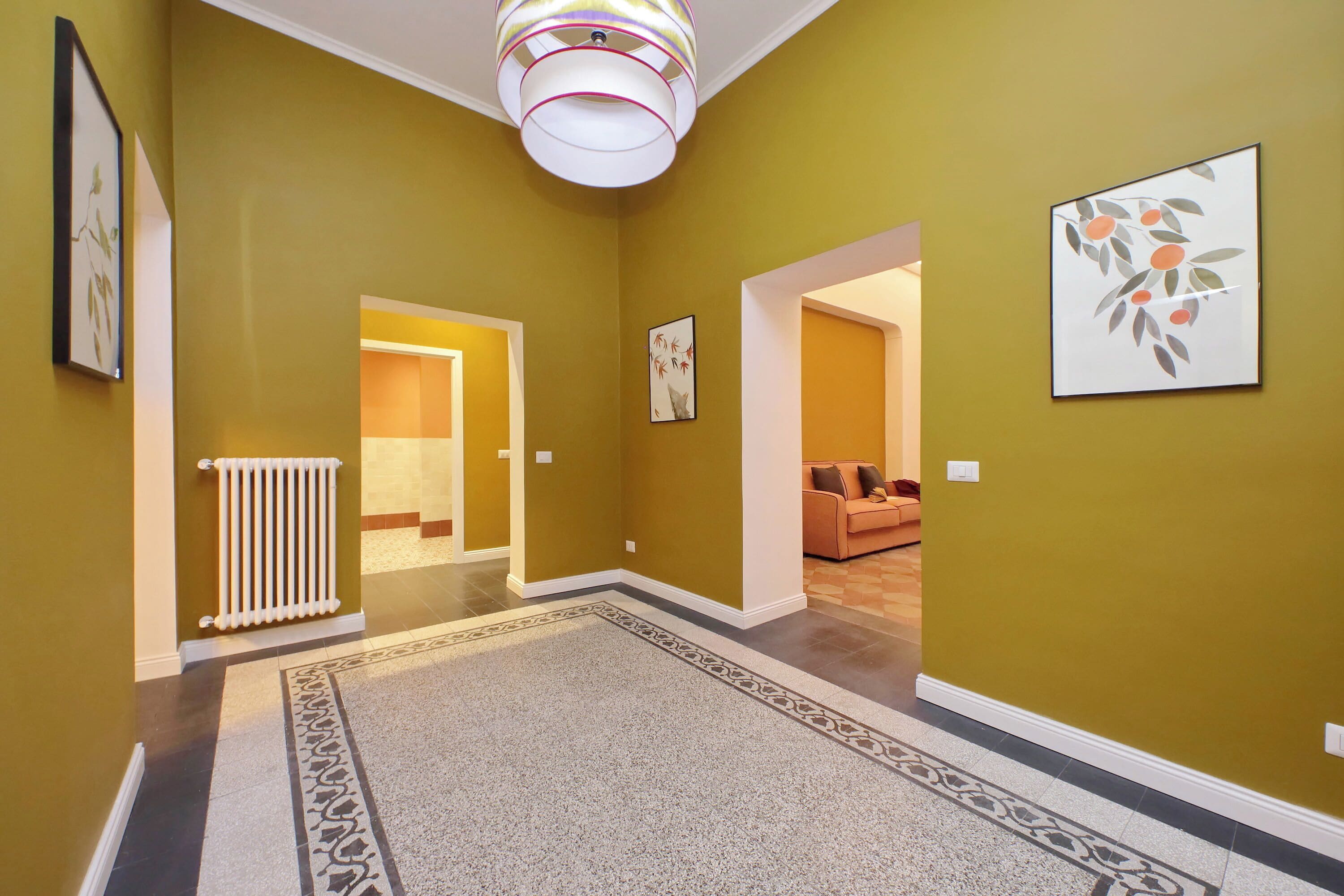 A hallway with a patterned rug, a radiator, and framed artwork on the walls.