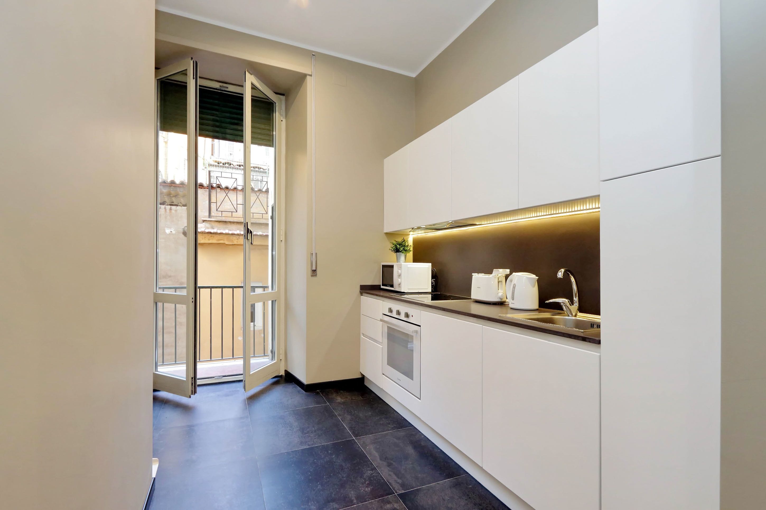 A modern kitchen with white cabinets, a built-in oven, a microwave, and a sink.