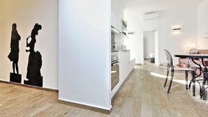 A modern kitchen with white cabinets, a stainless steel range hood, and a dining area with a table and chairs. - Monti Apartments - My Extra Home (Rome)