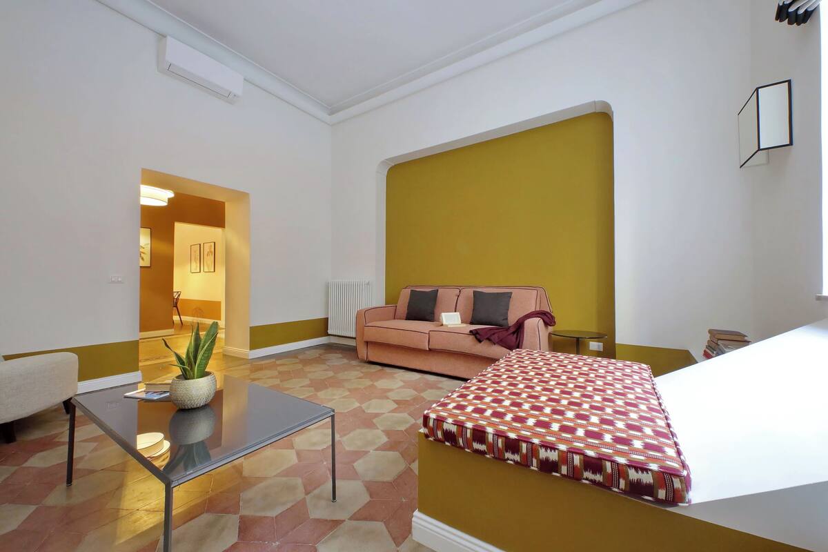 A modern living room with a sofa, a glass coffee table, and a patterned bedspread.