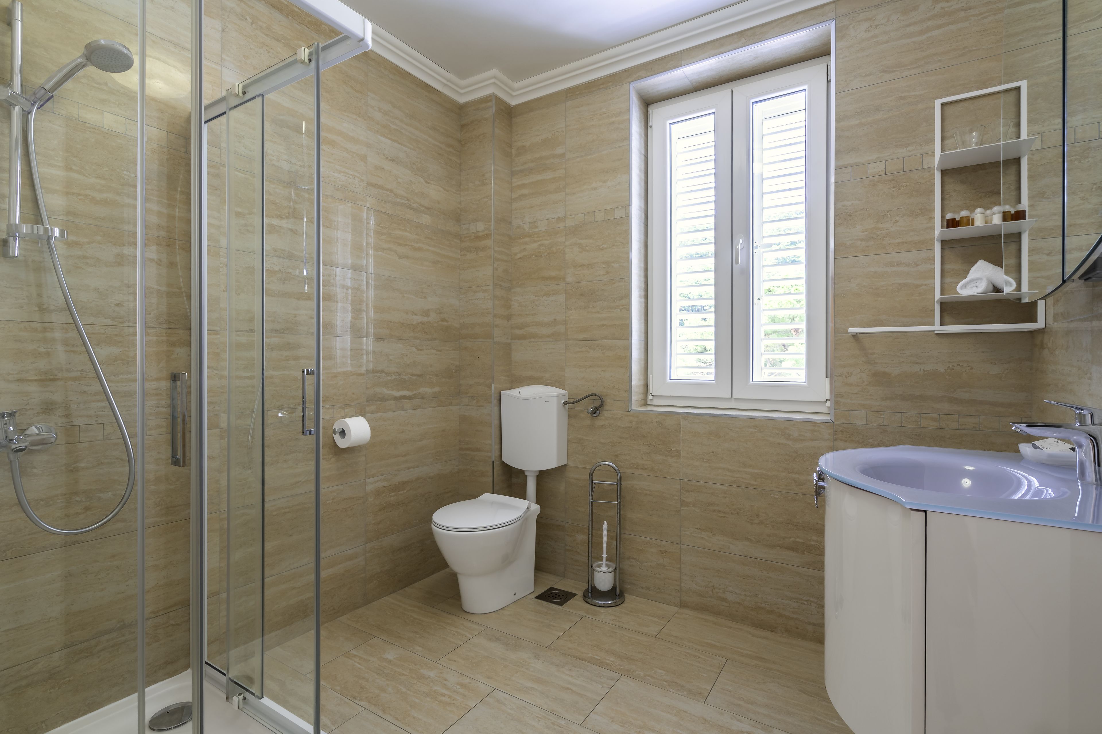 A bathroom with a glass shower enclosure, a toilet, a sink, and a window.