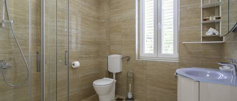 A bathroom with a glass shower enclosure, a toilet, a sink, and a window.