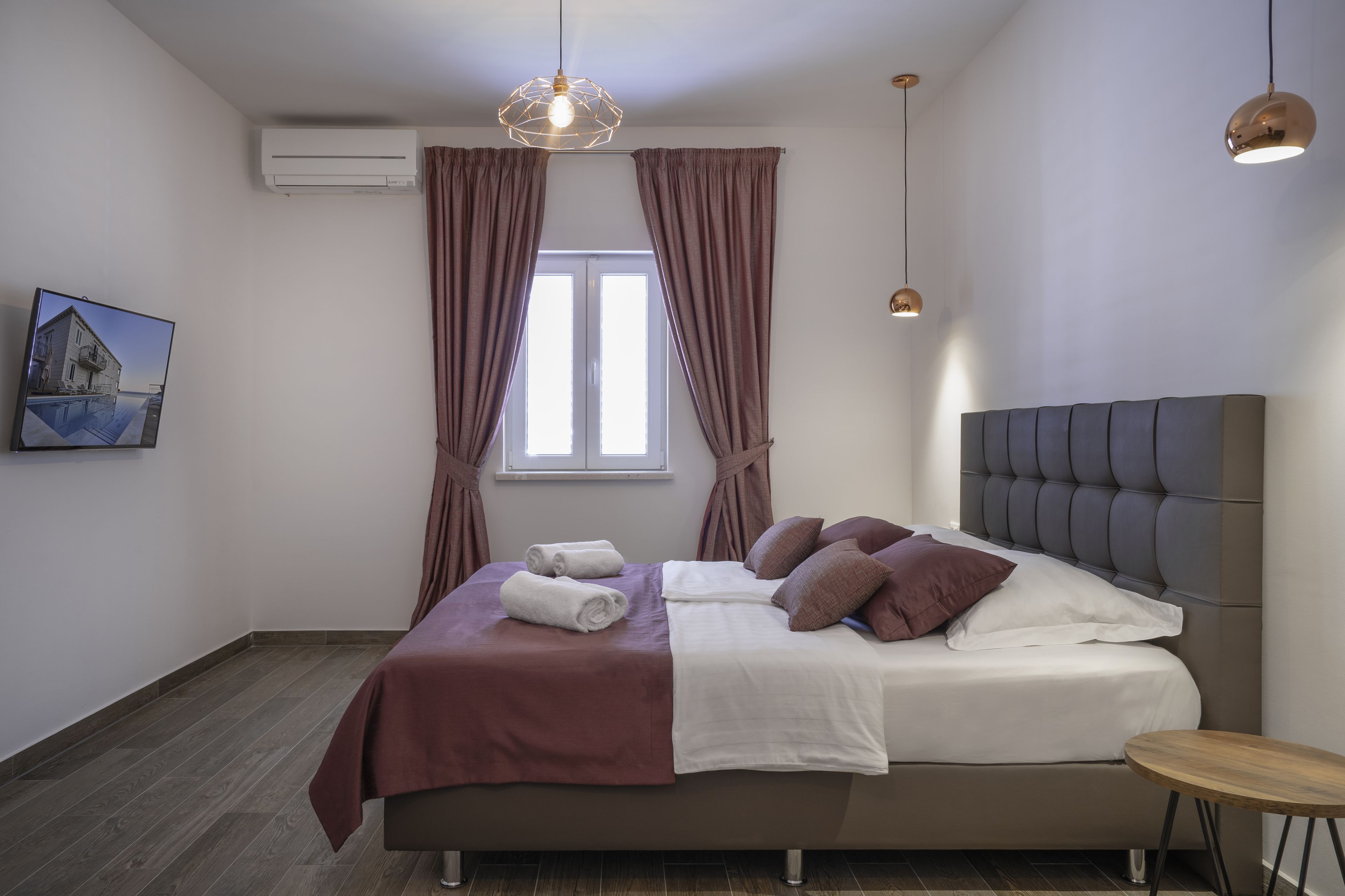A modern bedroom with a large bed, a small round table, and a window with curtains.