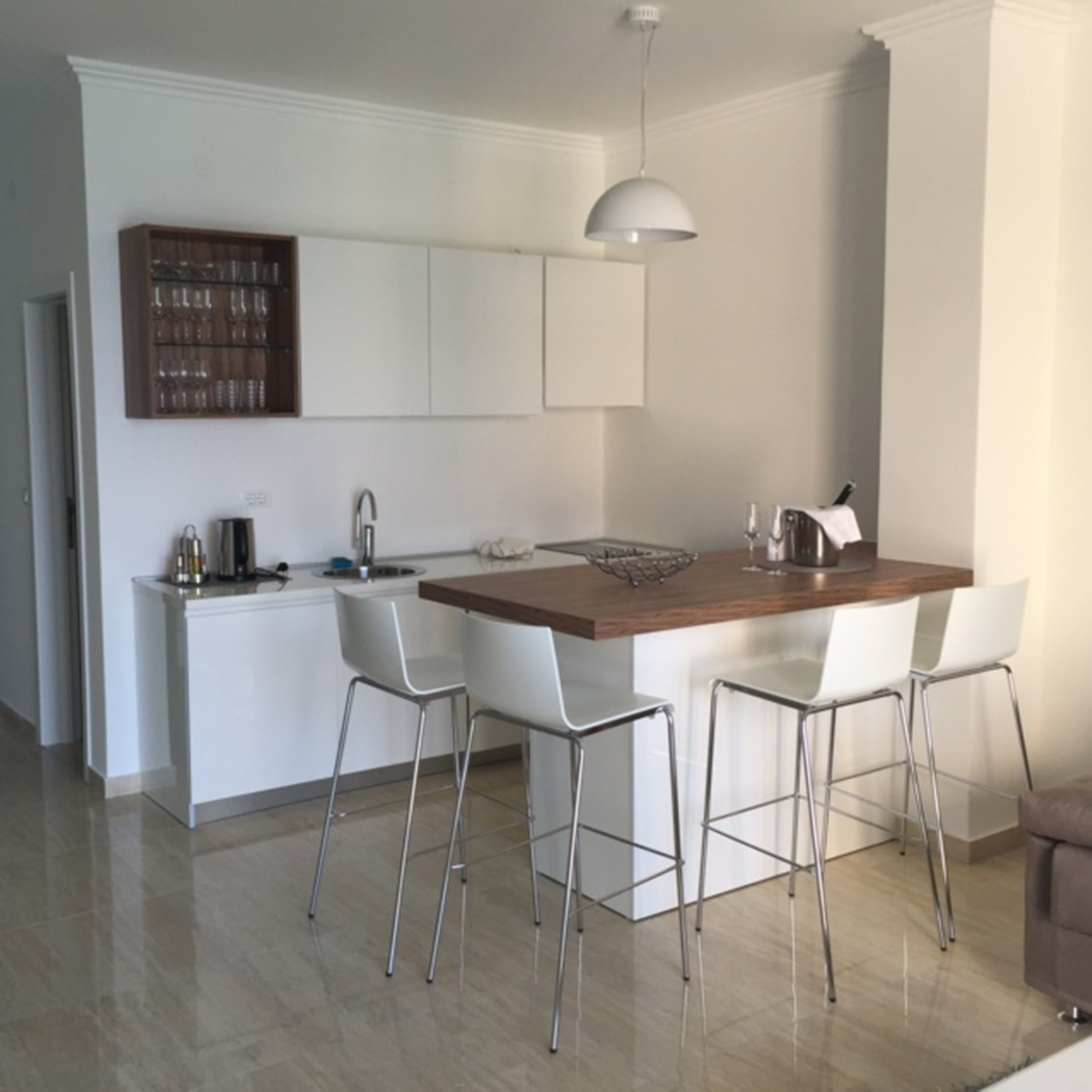A modern kitchen with white cabinetry, a wooden island, and bar stools.
