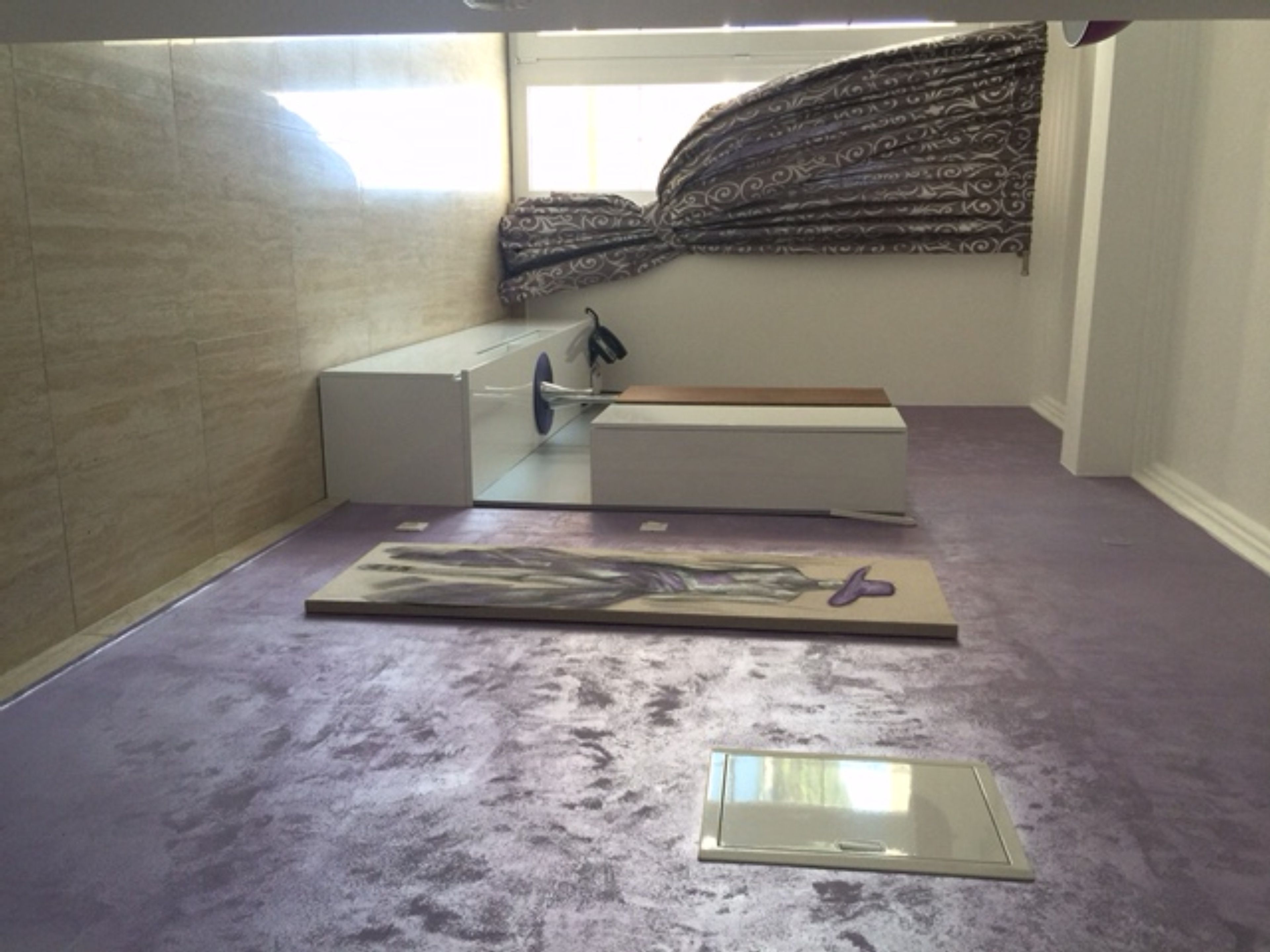 Una habitación con una cama, un mueble blanco pequeño, un ventanal con cortinas estampadas y una alfombra morada.