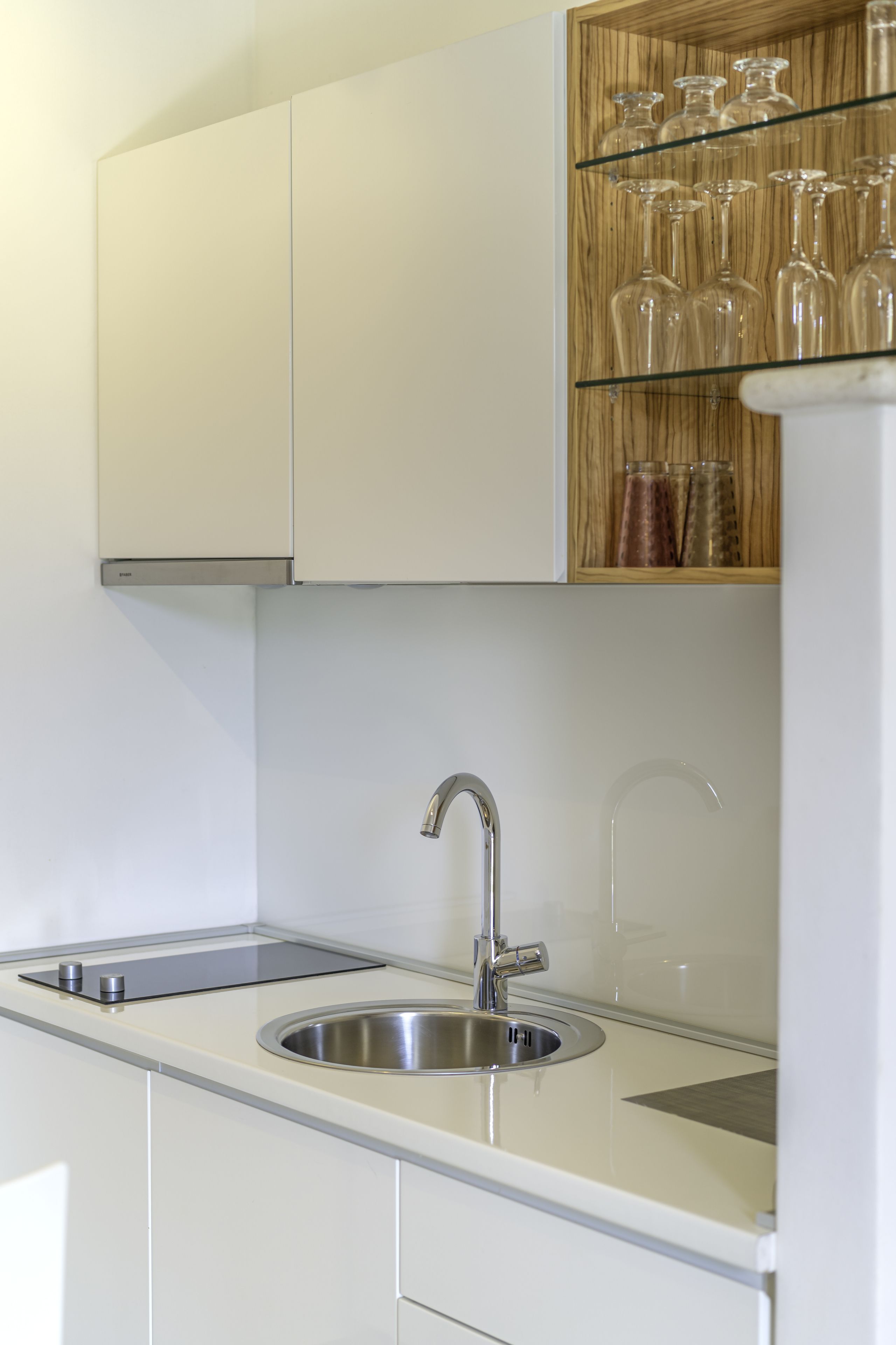 A modern kitchen with white cabinetry, a stainless steel sink, and a wooden spice rack.