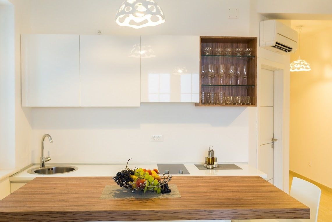 A modern kitchen with white cabinetry, a wooden dining table, and a fruit bowl.