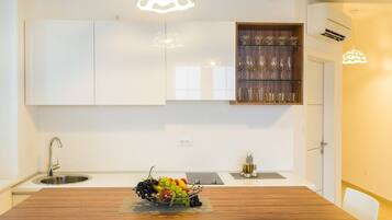 A modern kitchen with white cabinetry, a wooden dining table, and a fruit bowl.