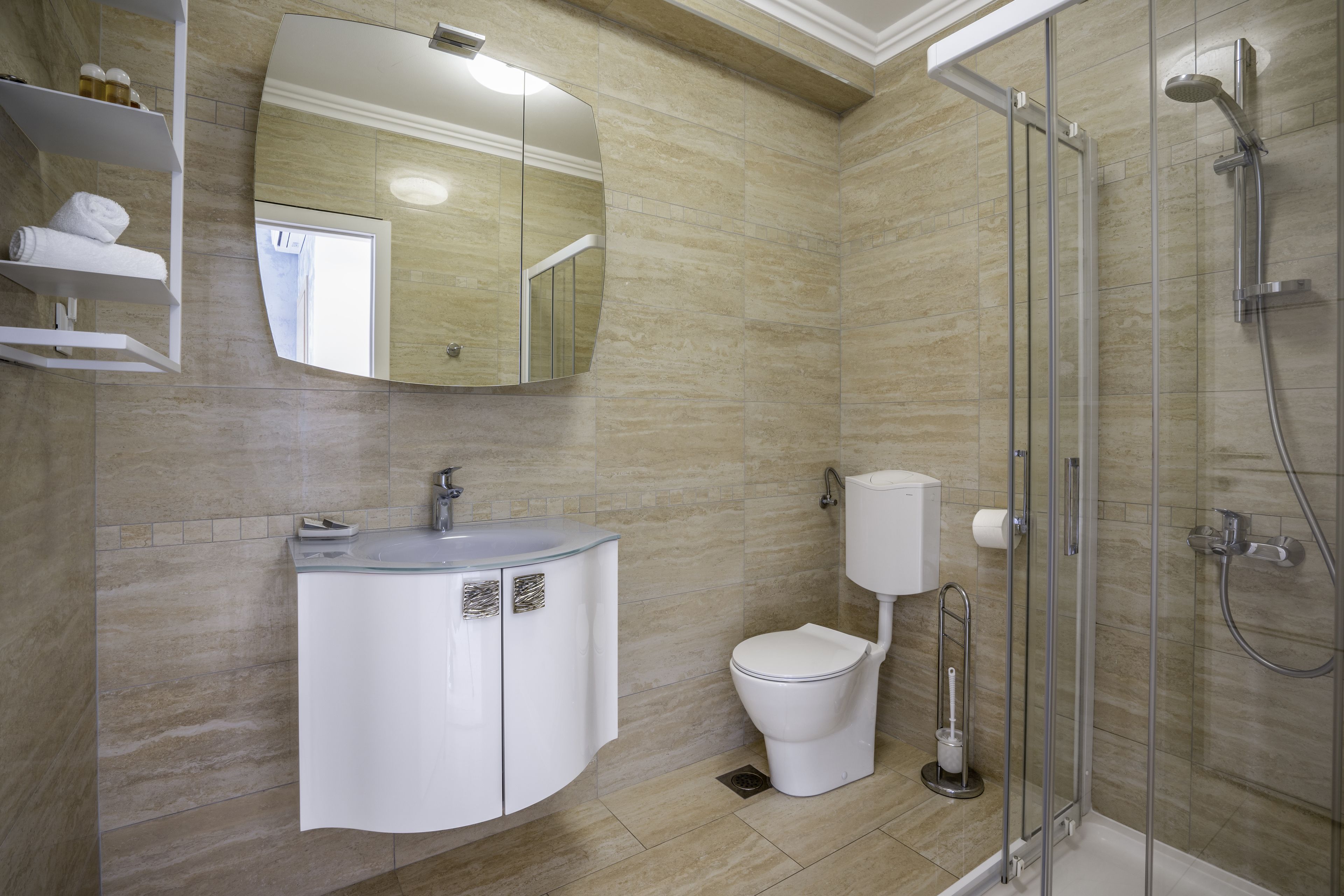 Et moderne badeværelse med en brusekabine i glas, en hvid vask med et spejl over og et toilet med hvid tank.