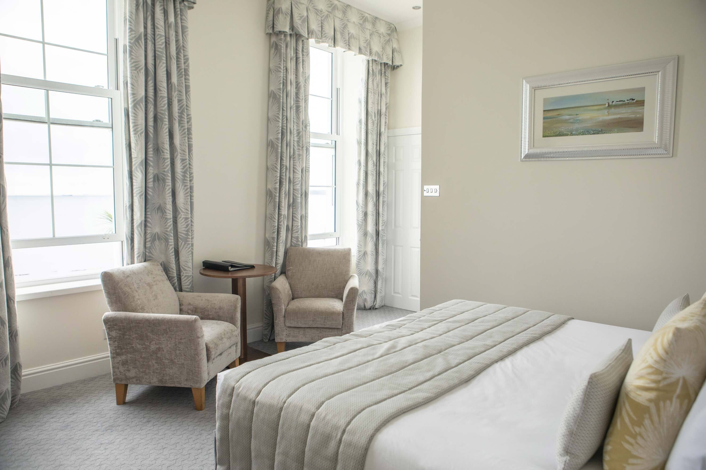 Camera d'albergo con un letto grande, due poltrone, un tavolino e un quadro appeso al muro.