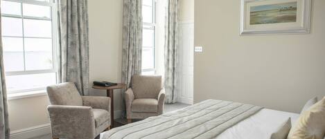 A hotel room with a large bed, two armchairs, a small table, and a painting on the wall.