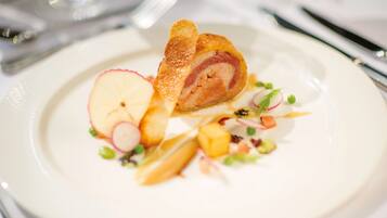 A plate with a rolled meat dish, apple slices, radish, and green peas.