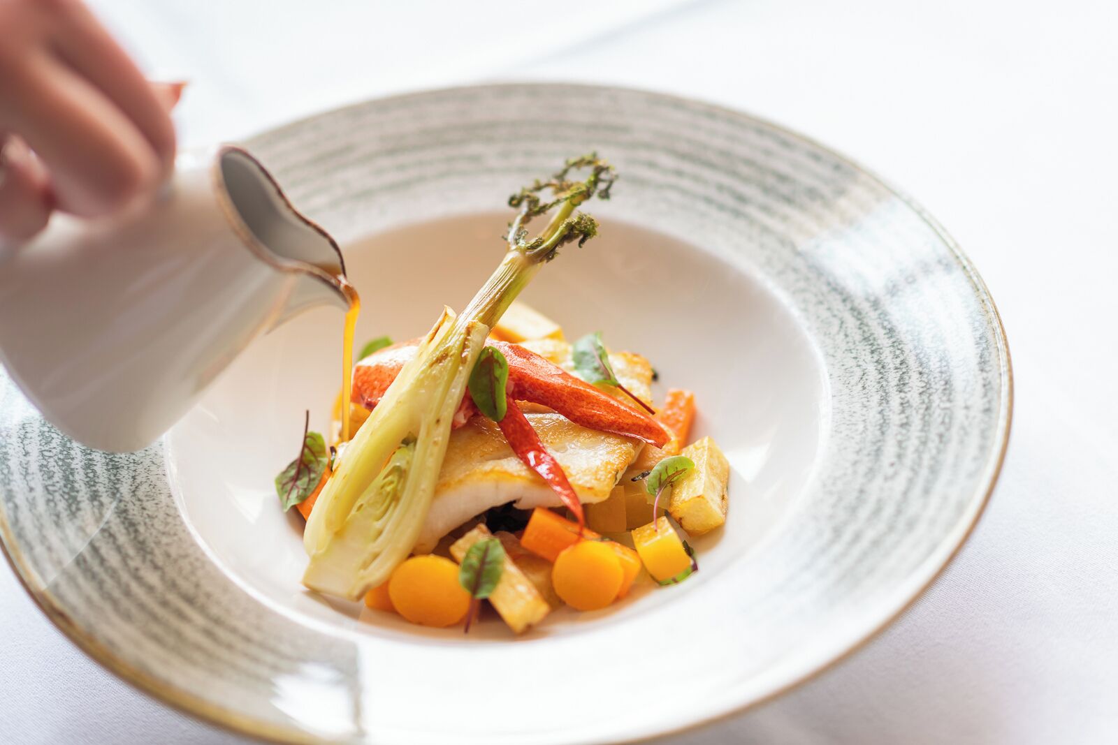 A white plate with a fish fillet, vegetables, and a garnish.
