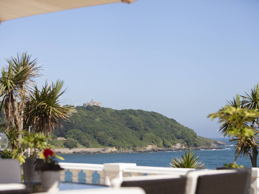 A seaside view with a hill, palm trees, and a building on top.