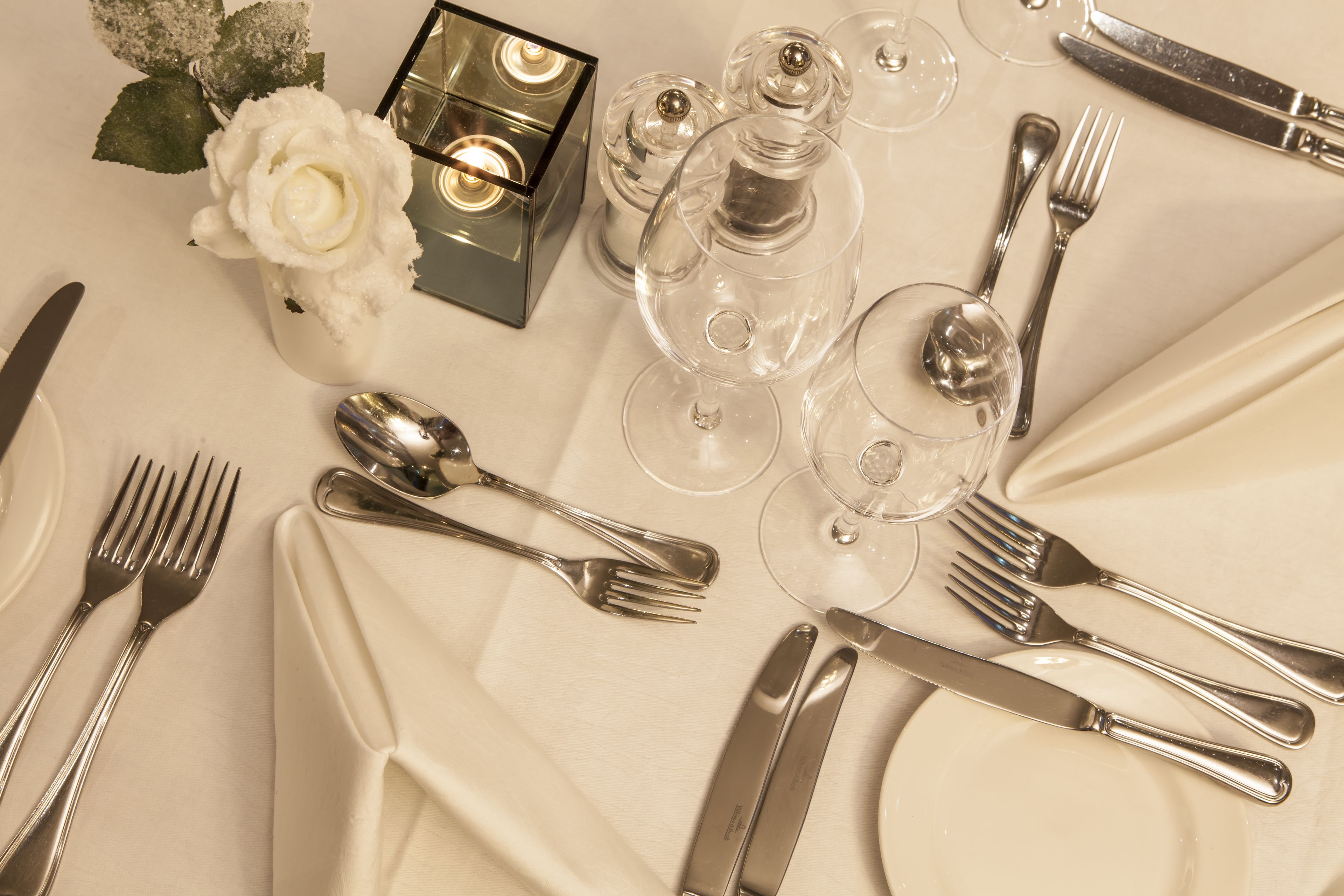 A table set for a formal dinner with silverware, plates, and clear glassware.