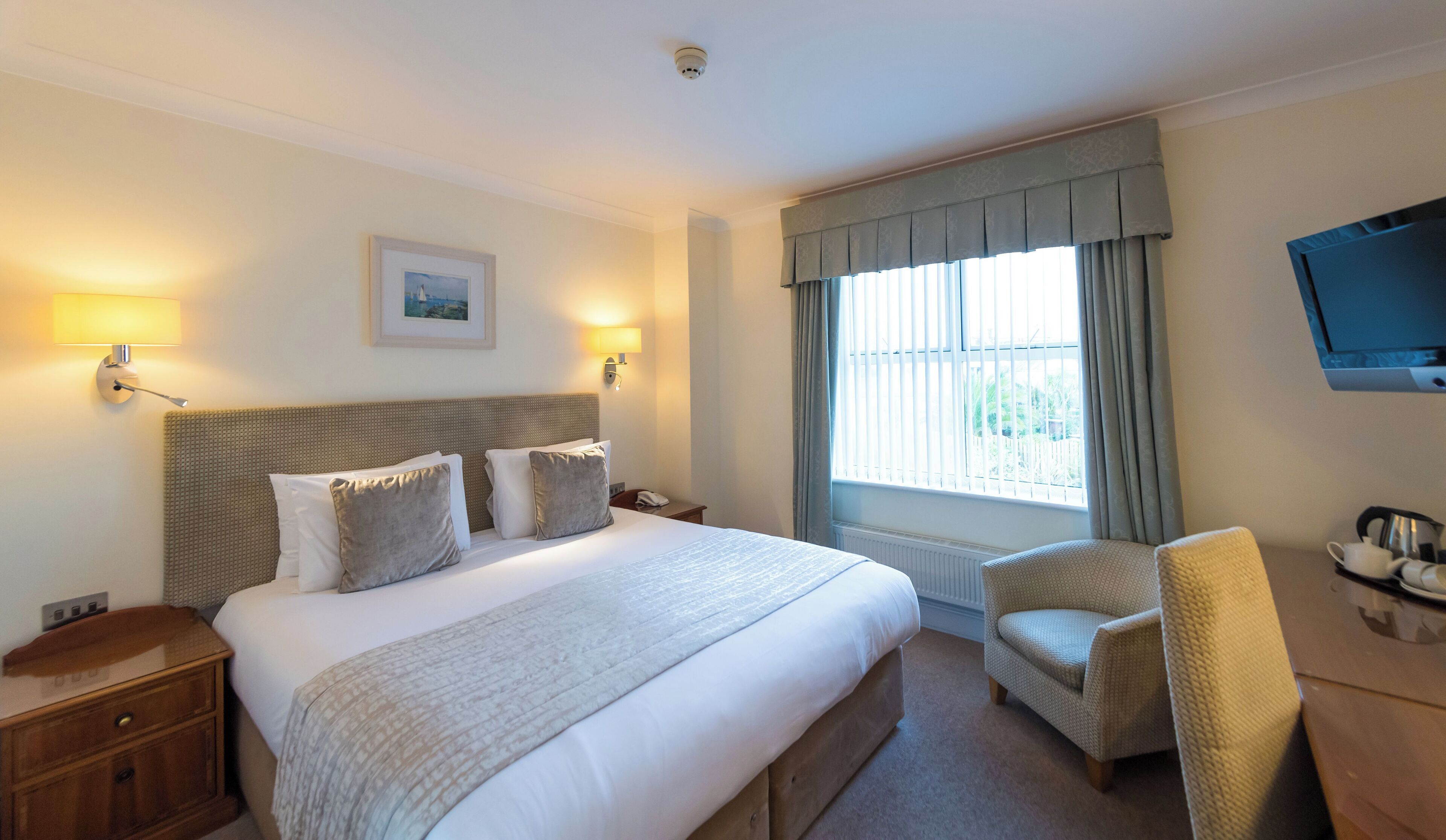 A hotel room with a large bed, two bedside lamps, a television, a chair, and a window with curtains.
