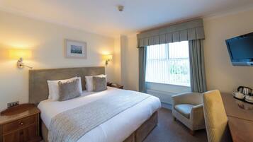 A hotel room with a large bed, two bedside lamps, a television, a chair, and a window with curtains.