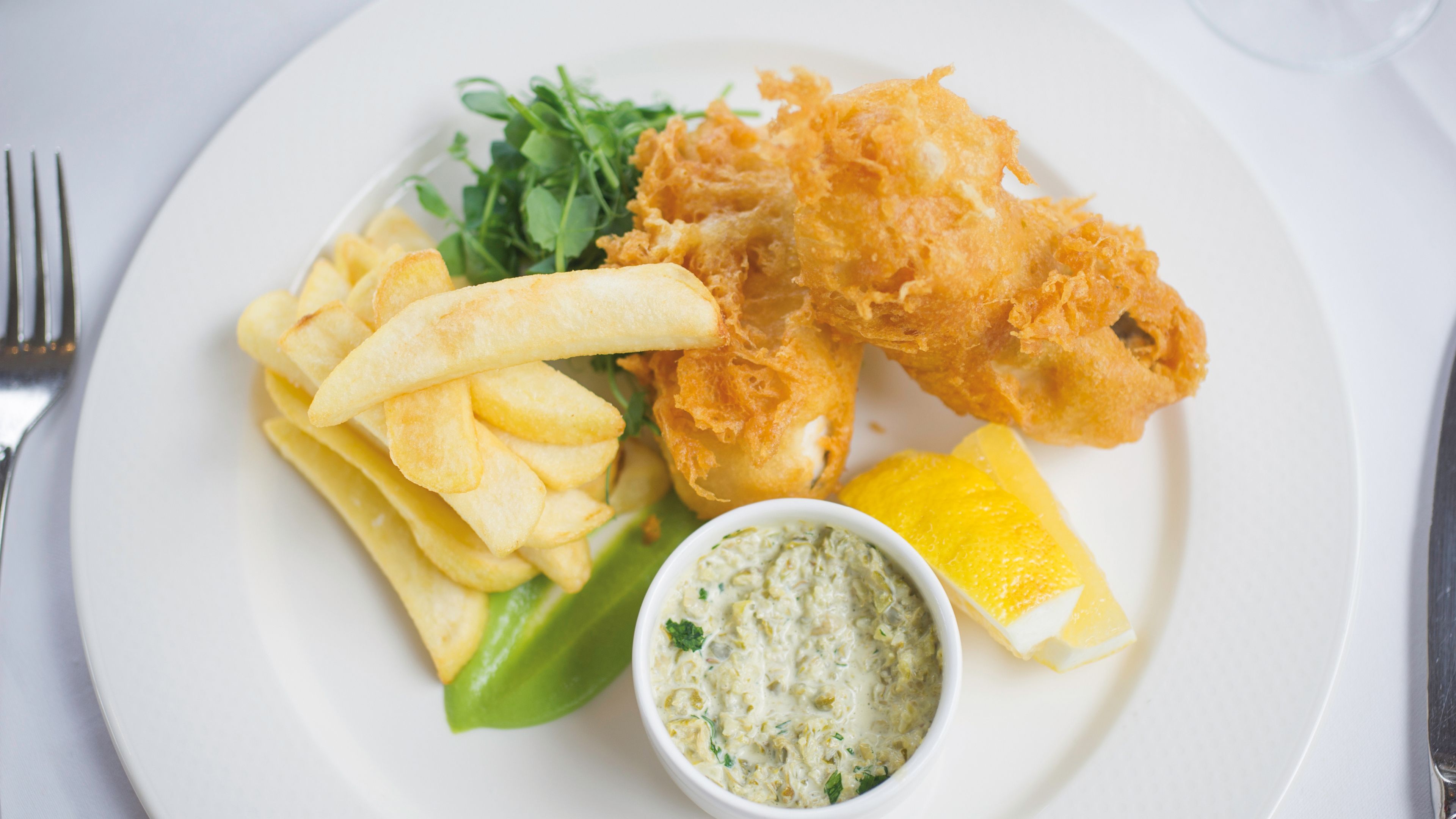 A plate with fried fish, chips, a lemon wedge, and a side salad.