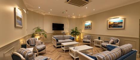 A spacious lounge area with striped sofas, a flat-screen TV, and a large potted plant.