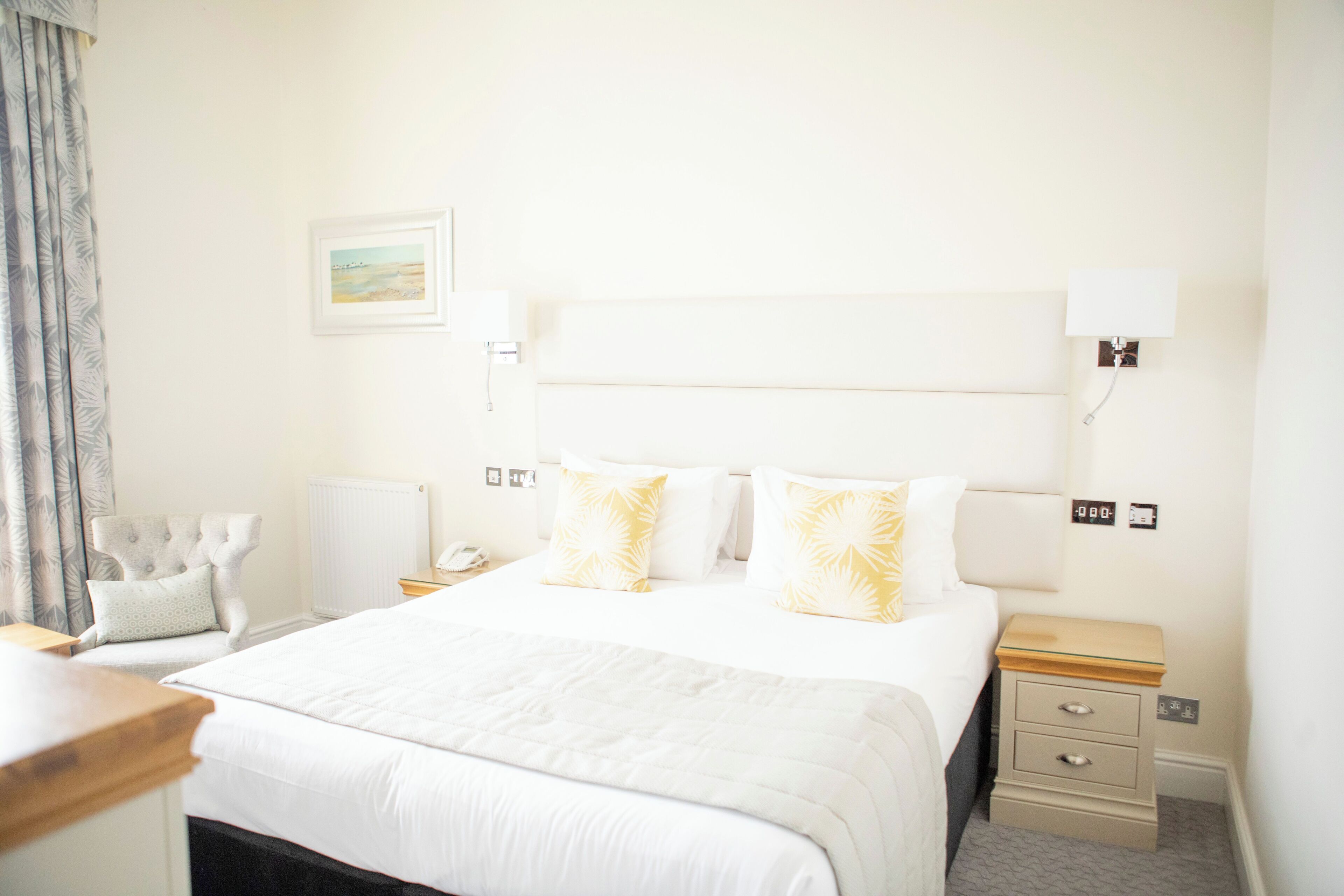A hotel room with a large bed, bedside tables, a chair, and a nightstand with a lamp.