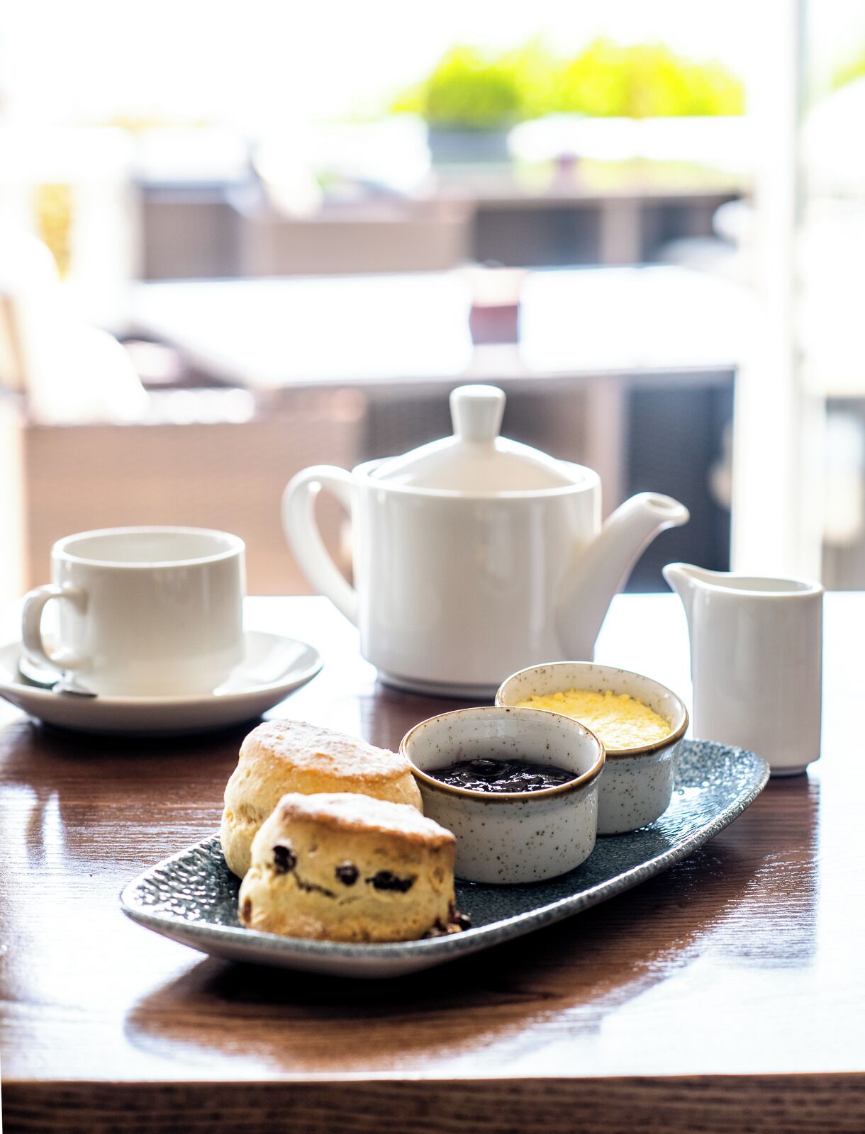 A table with a teapot, cups, a jug, and a plate with scones and jam.