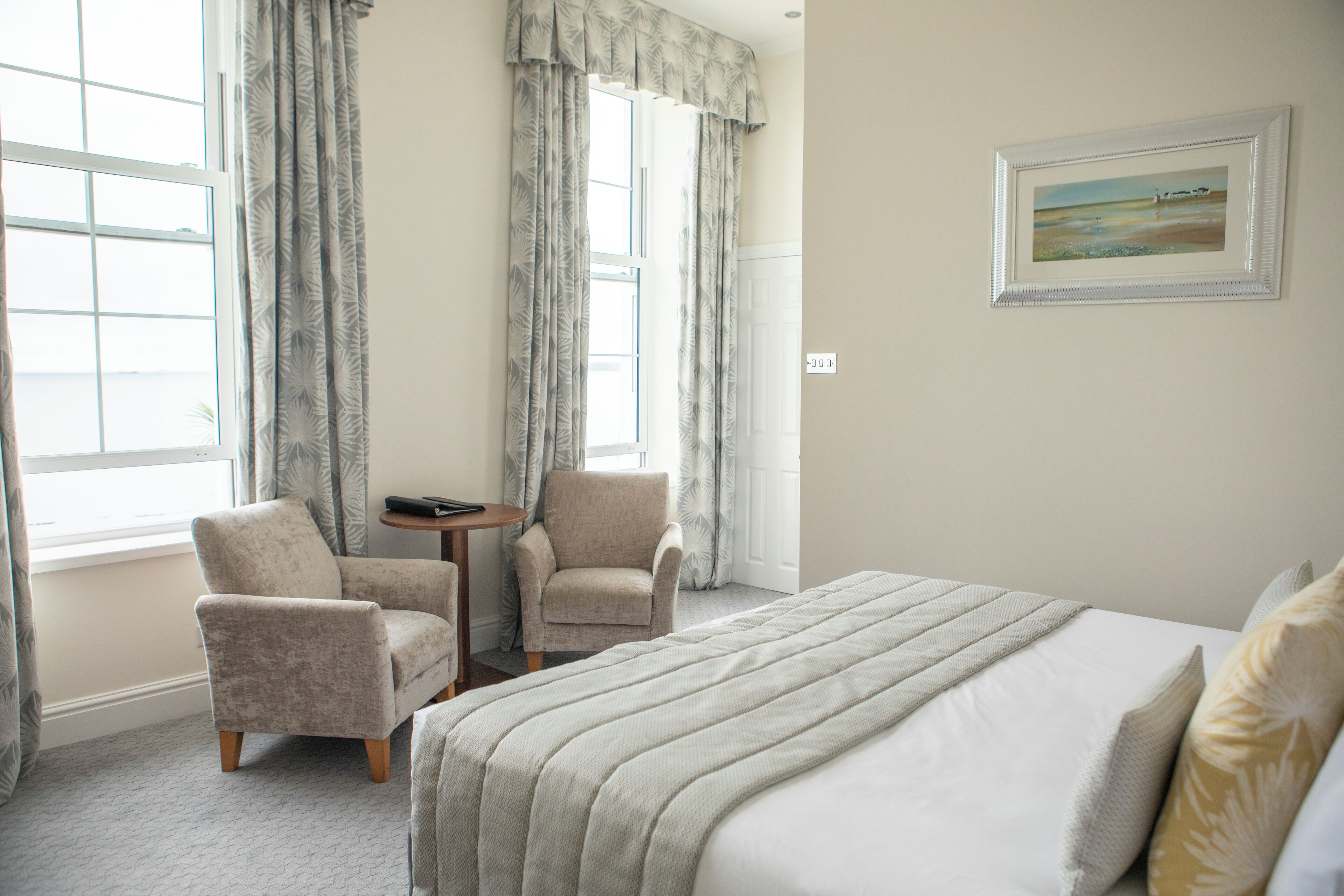 A hotel room with a large bed, two armchairs, a small table, and a painting on the wall.