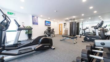 A gym with treadmills, weight machines, and a TV screen displaying a fitness program.