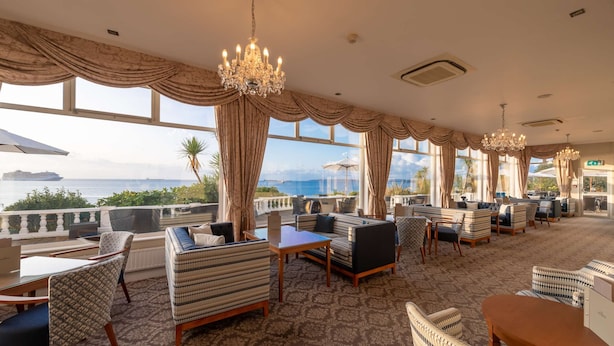 A spacious lounge area with multiple seating options, large windows offering ocean views, and elegant chandeliers. - The Royal Duchy Hotel (Falmouth)