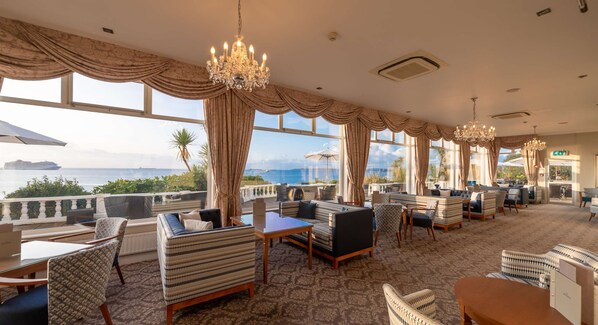 Ett rymligt loungeområde med flera olika sittplatser, stora fönster med utsikt över havet och eleganta kristallkronor.