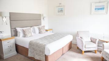 A neatly arranged bedroom with a large bed, bedside tables, a chair, and framed pictures on the wall.
