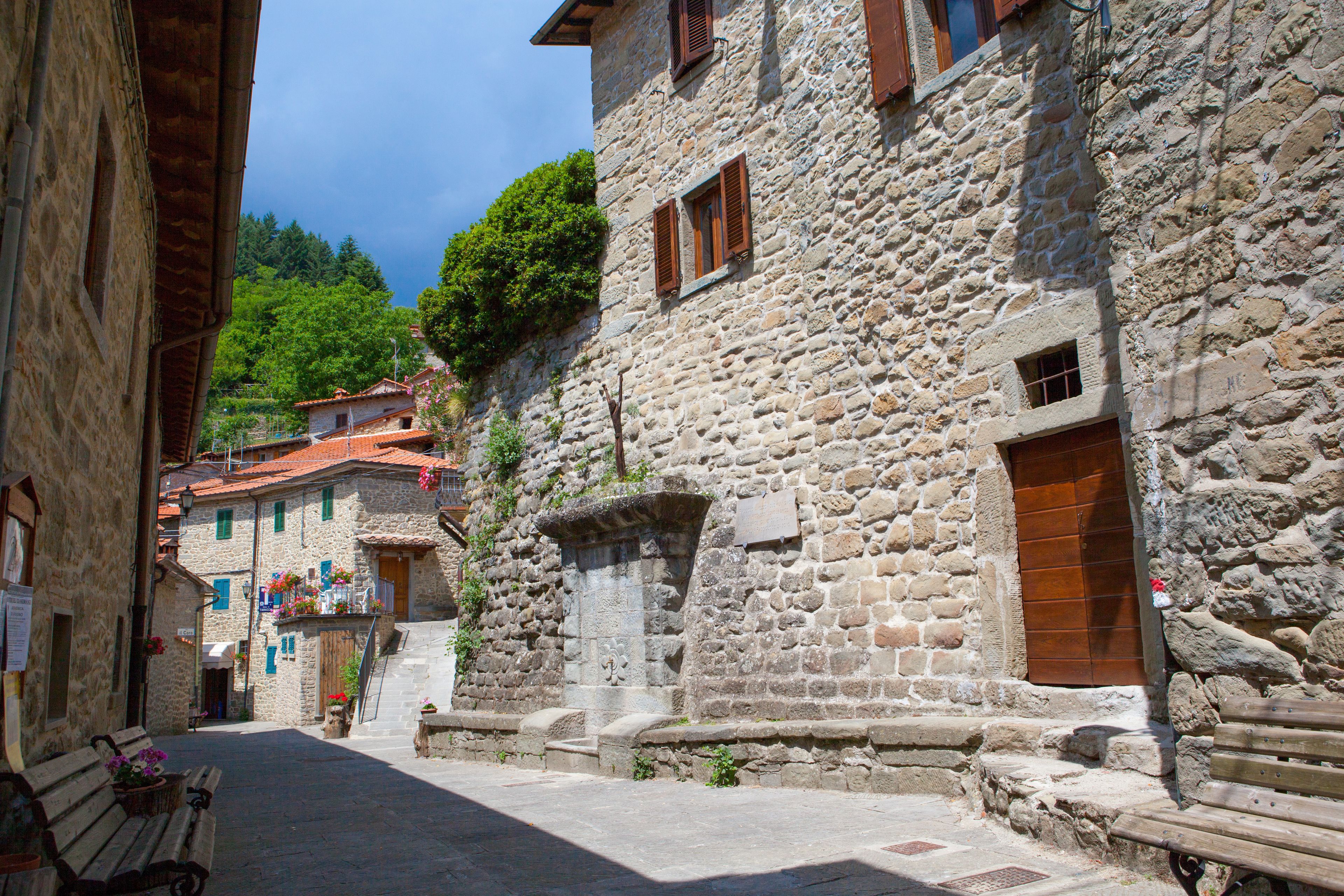 A narrow cobblestone street lined with stone buildings, wooden benches, and flower boxes.