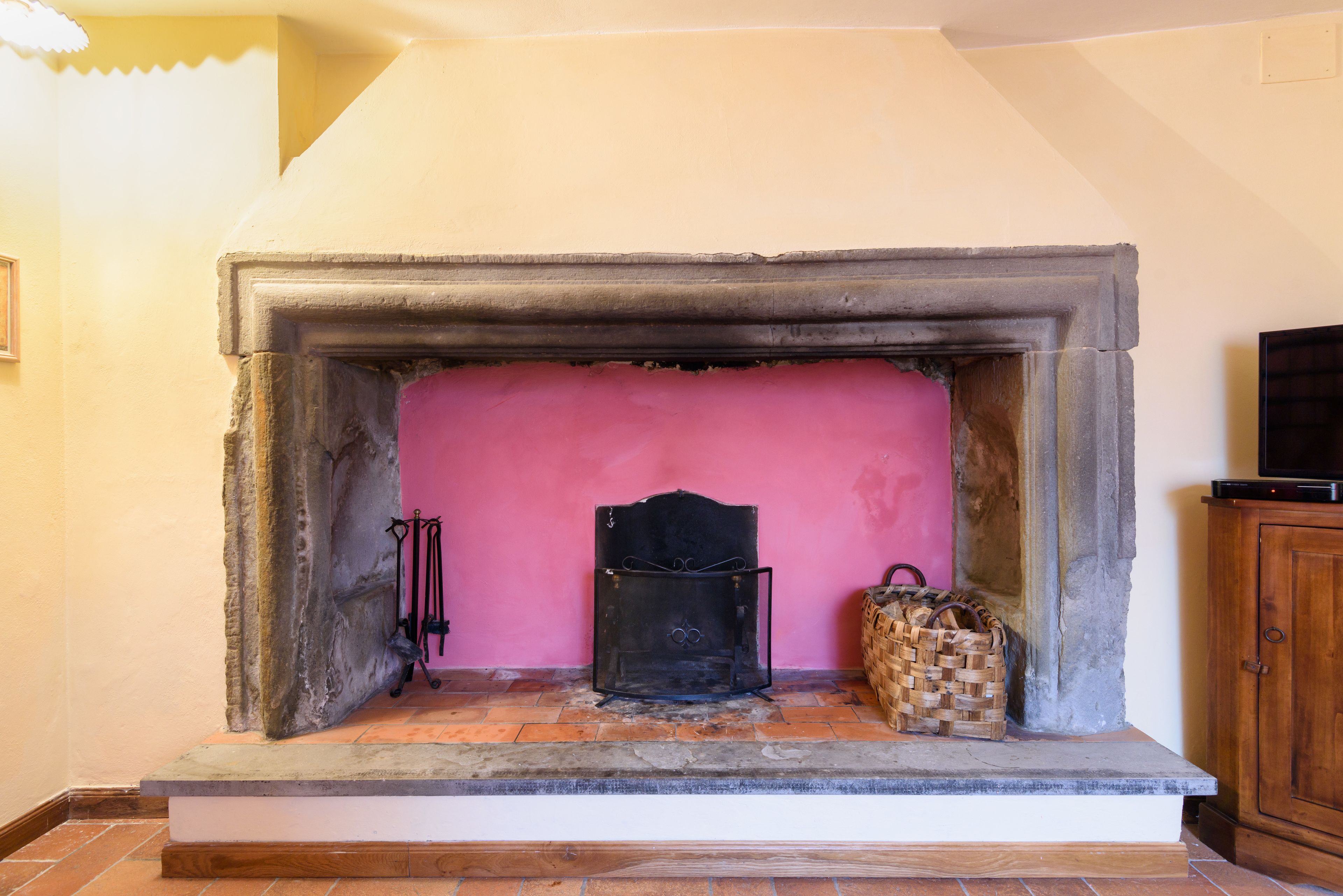 A fireplace with a stone surround, a pink wall behind it, and a woven basket on the hearth.