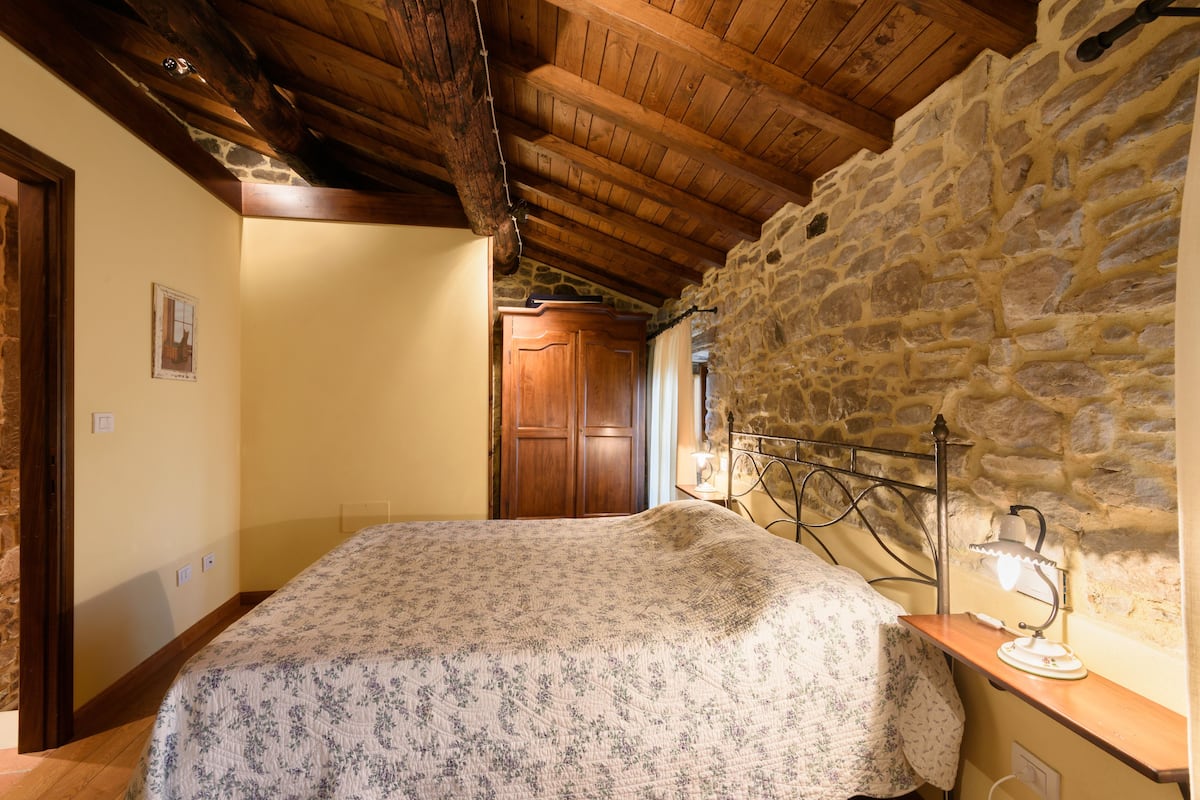 A bedroom with a wooden ceiling, stone wall, and a bed with a floral bedspread.