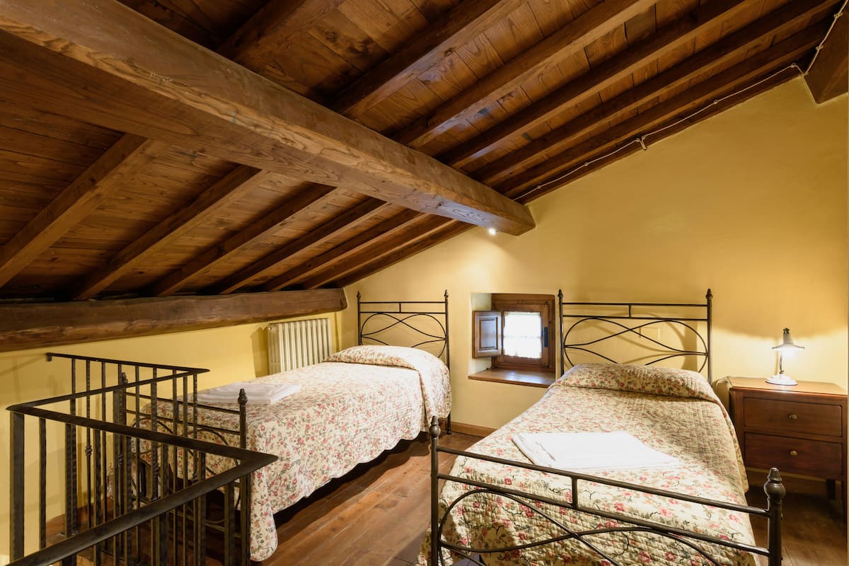 A bedroom with two beds, wooden beams, a window, and a nightstand.