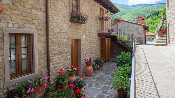 Ein Gebäude aus Stein mit einer Holztür, Fenstern mit Fensterläden und Blumentöpfen mit Blumen.