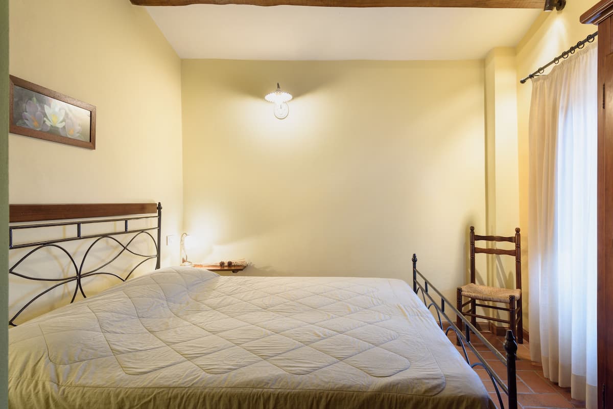 A bedroom with a bed, a chair, a nightstand, and a painting on the wall.
