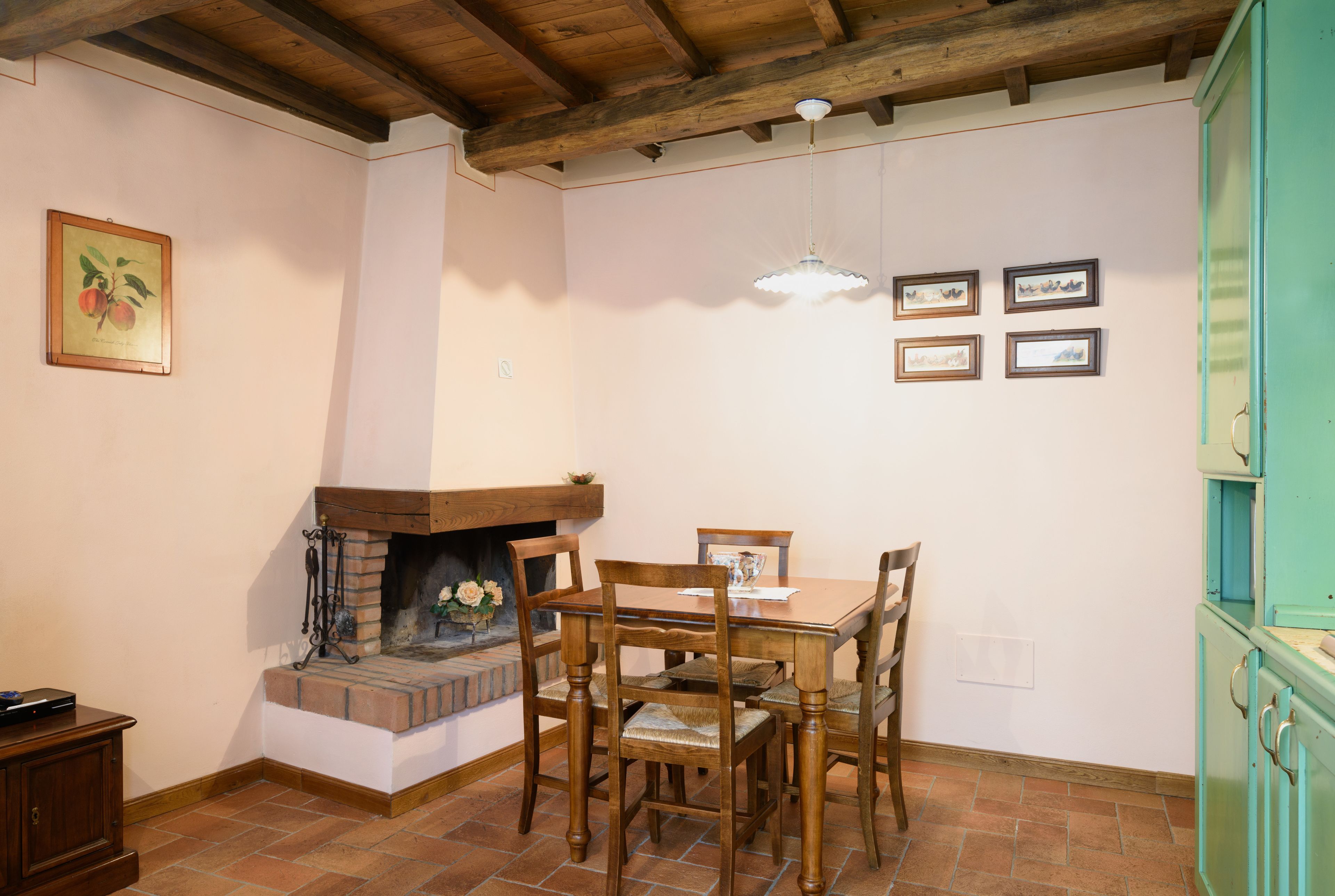 A dining area with a wooden table and chairs, a fireplace, and a hanging light fixture.