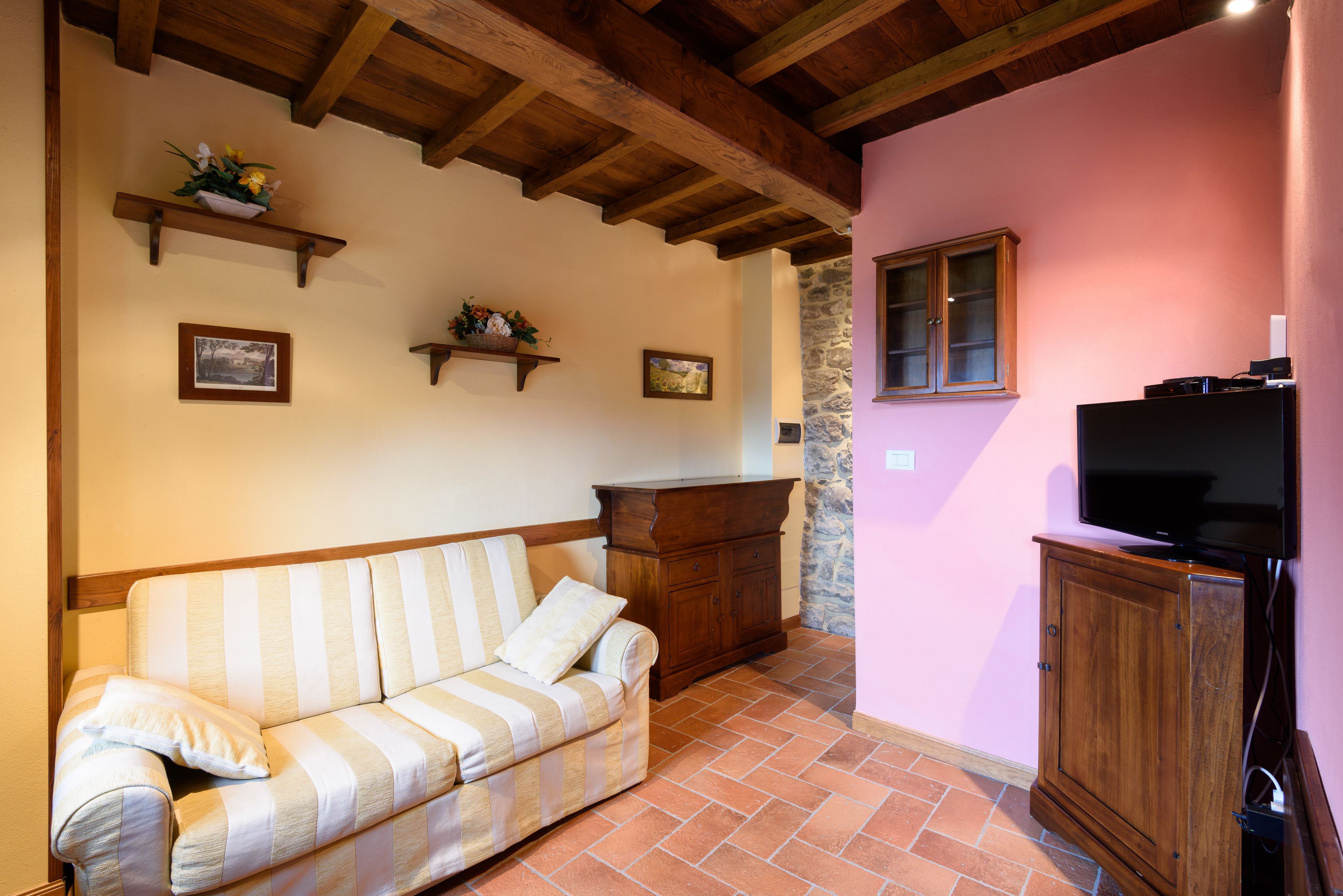 A living room with a striped sofa, wooden beams, a stone wall, a cabinet, and a television.