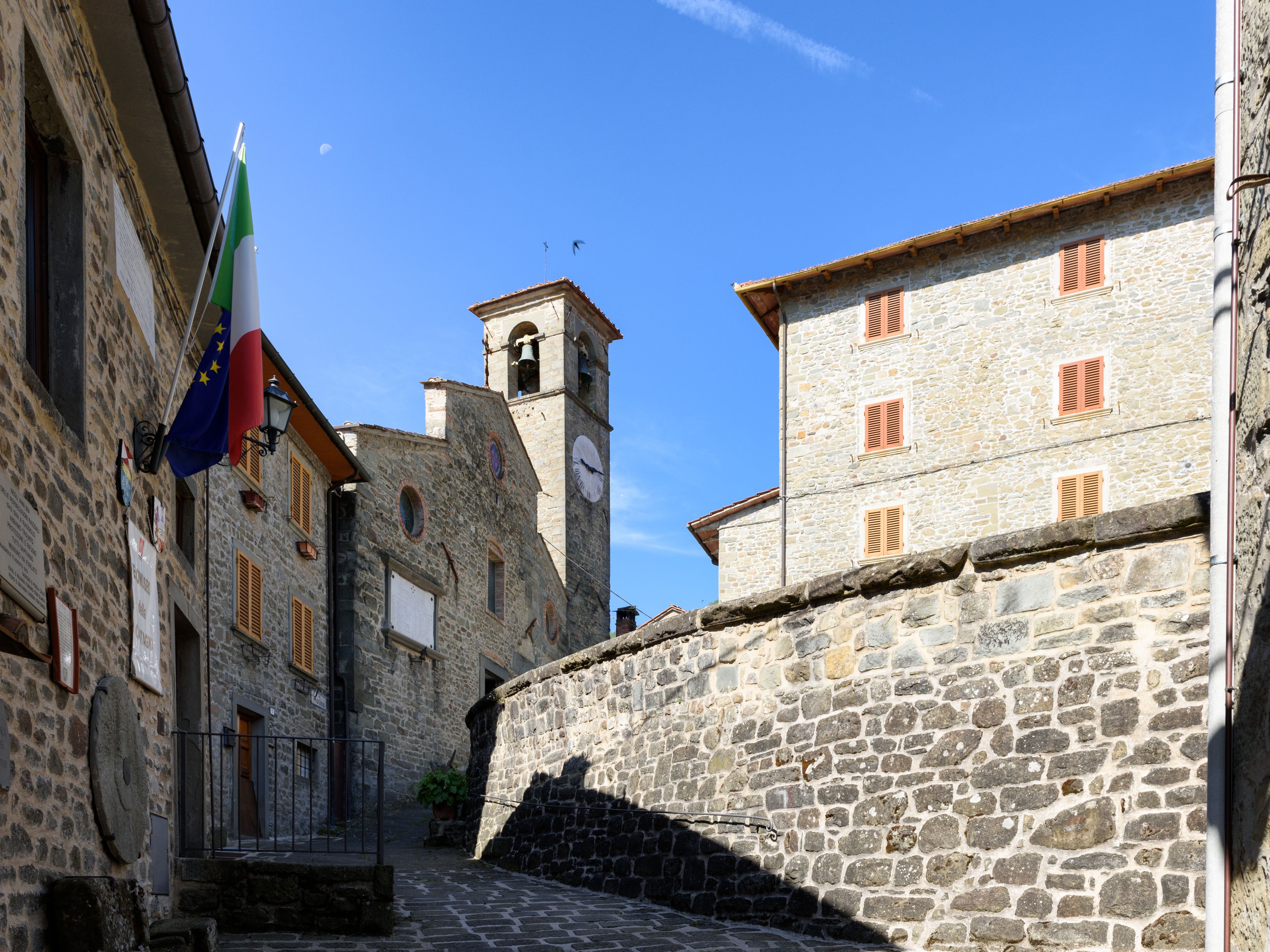 Un edificio de piedra con una torre de campanas, una bandera y una calle empedrada.