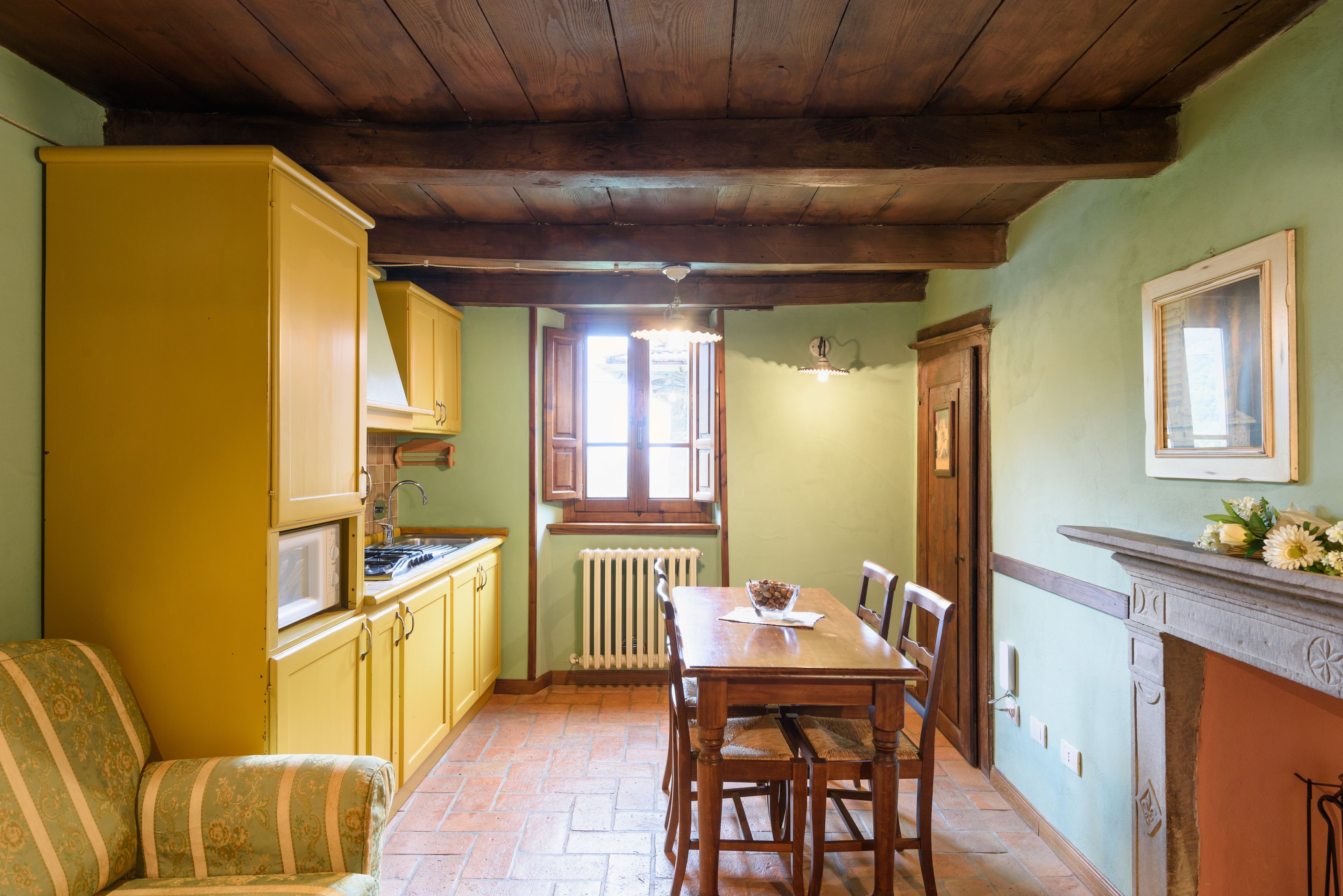 A dining area with a wooden table and chairs, yellow cabinets, and a radiator.