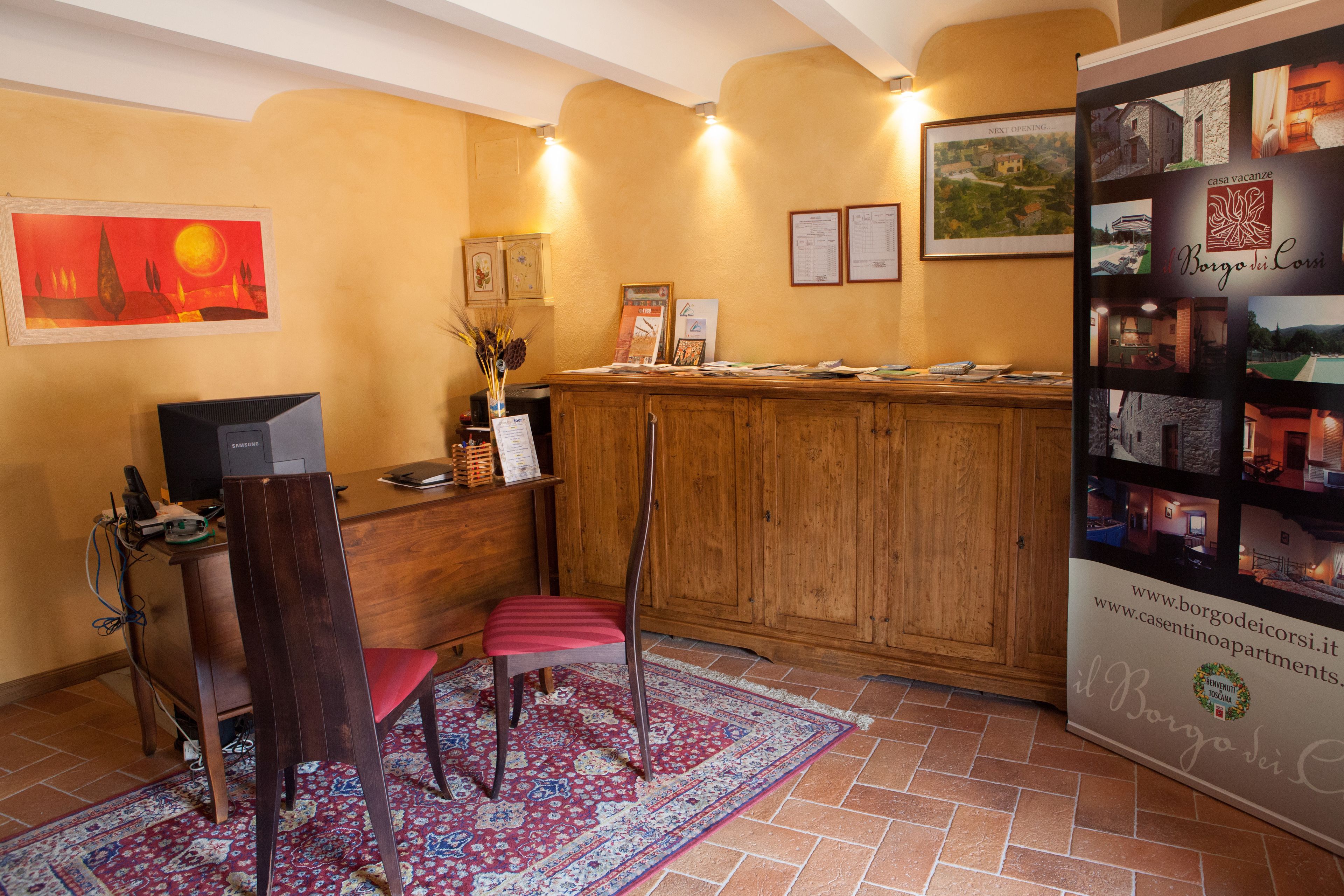 A reception area with a wooden desk, a computer, a telephone, and a chair. There is a framed painting on the wall and a bulletin board with papers.