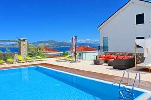 En swimmingpool med utsikt över havet, en vit byggnad och utomhusmöbler.