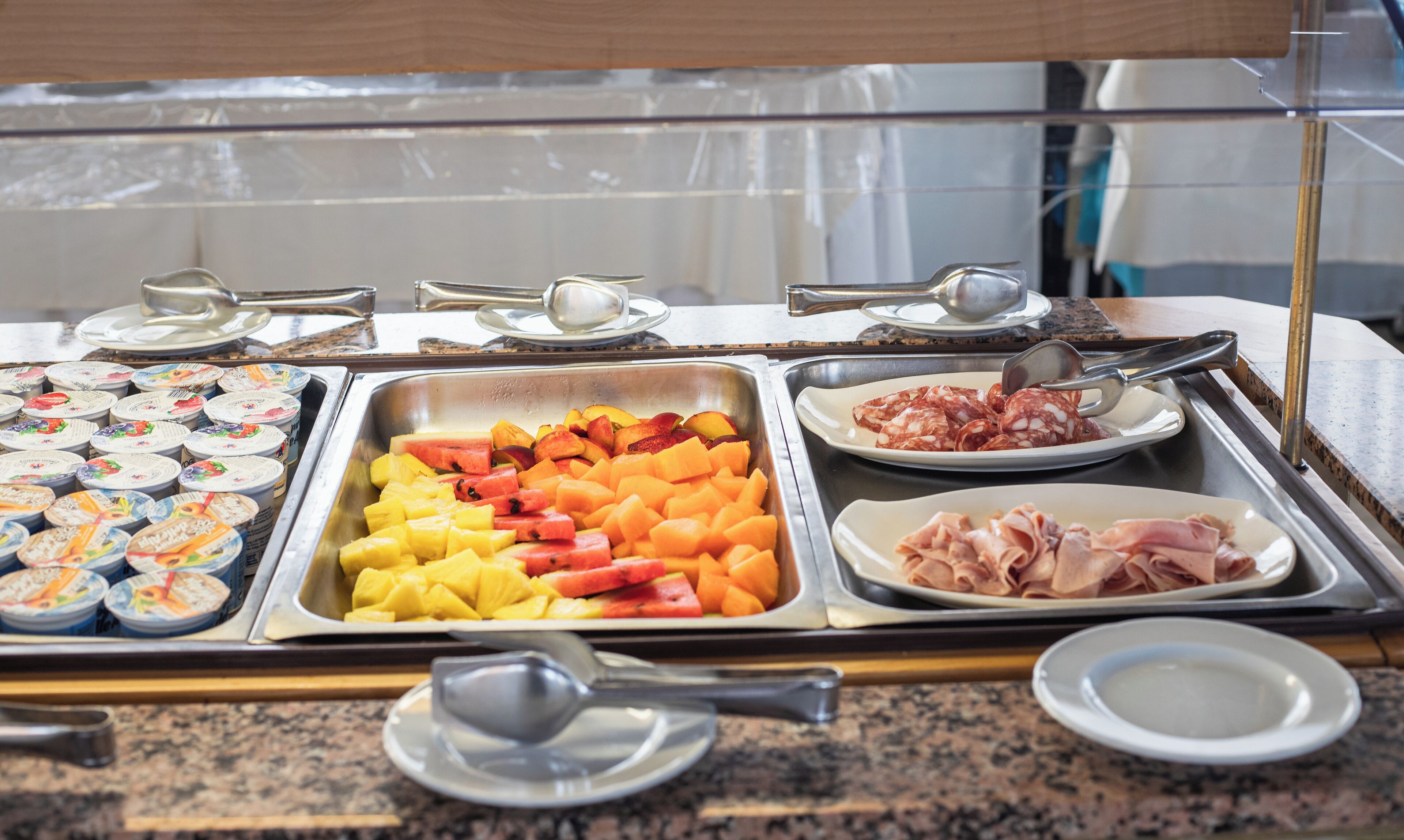 Buffet com diversos alimentos, incluindo frutas, iogurte e carnes.