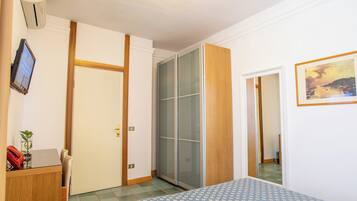 A bedroom with a bed, a desk, a chair, a wardrobe, and a painting on the wall.