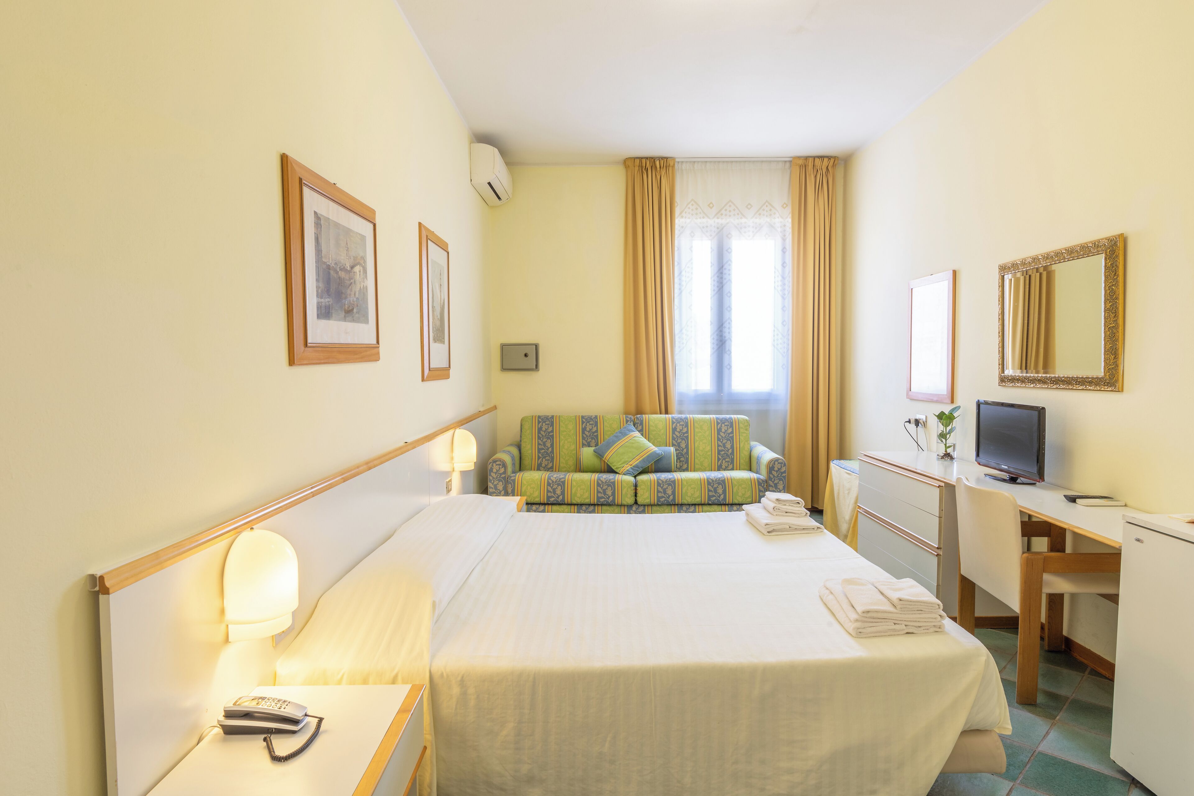 Camera d'albergo con un letto, una scrivania, una sedia, una televisione e una finestra con tende.