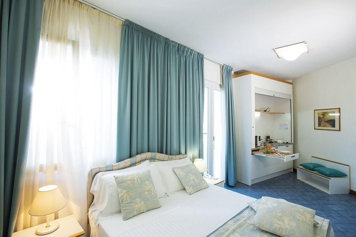 A hotel room with a bed, bedside table, and a small desk area with a chair.