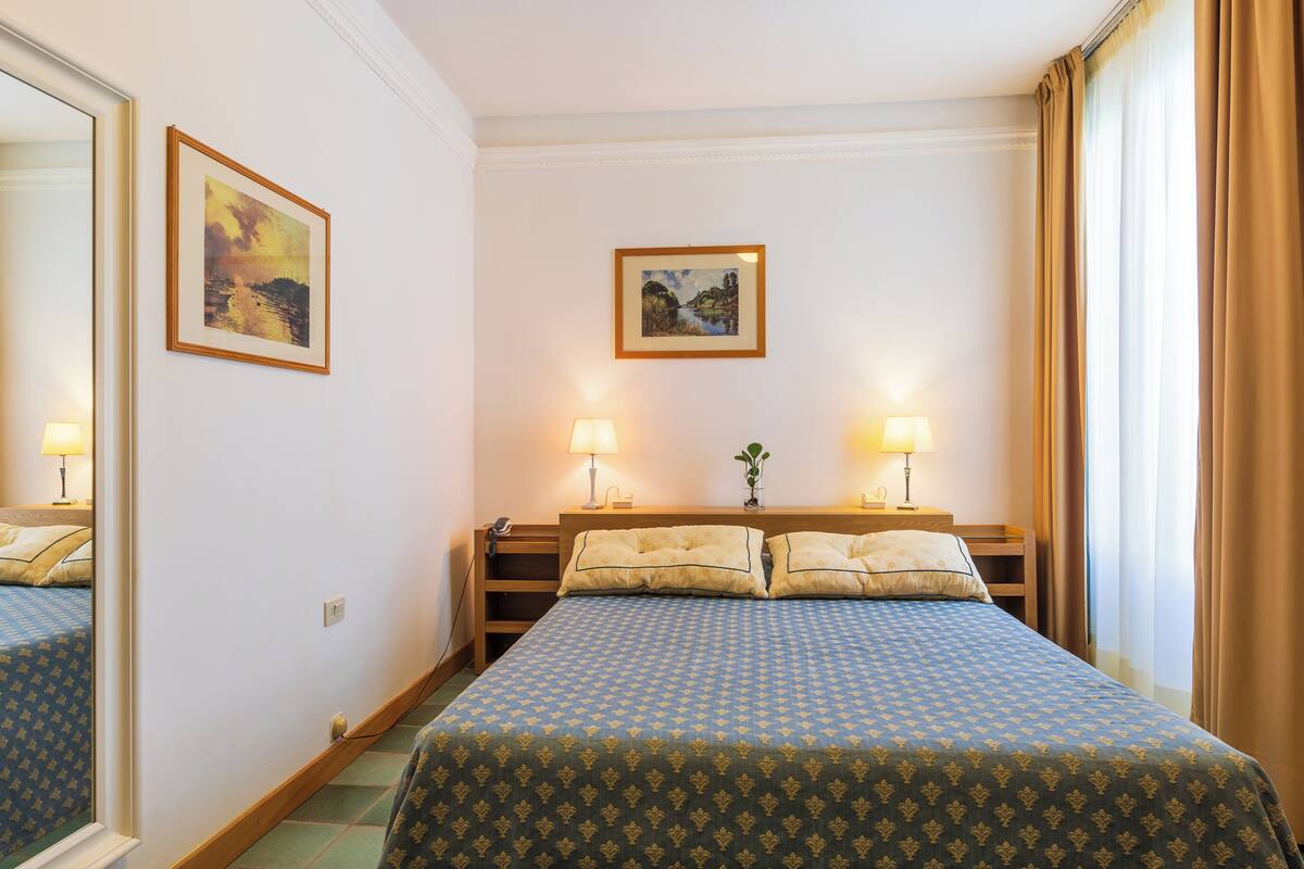 A hotel room with a bed, two bedside tables, lamps, and two framed pictures on the wall.