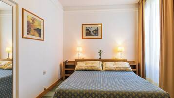 Une chambre d’hôtel avec un lit, deux tables de chevet, des lampes et deux tableaux encadrés accrochés au mur.