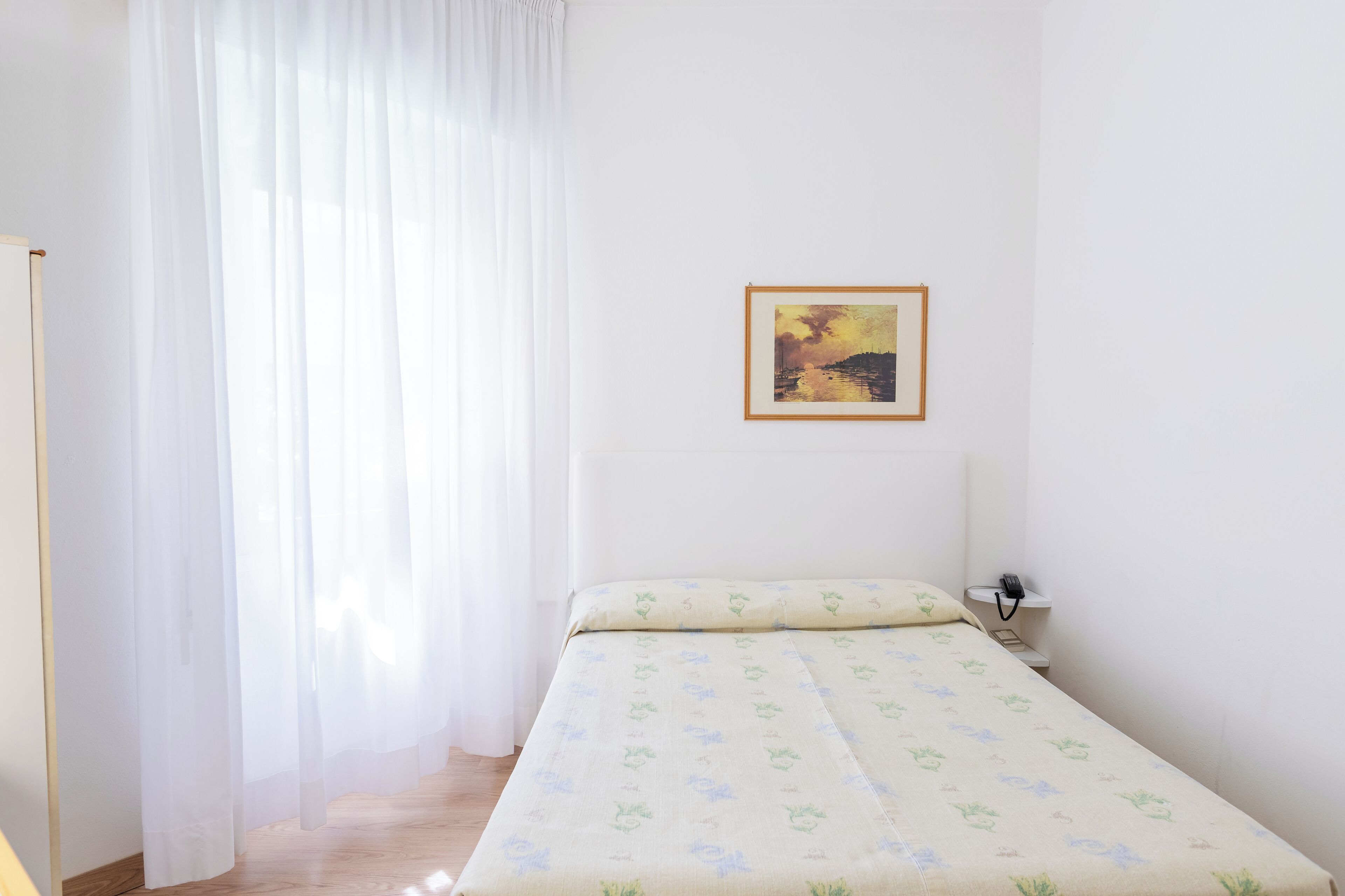 A single bed with a patterned bedspread, a bedside table with a phone, and a framed picture on the wall.
